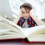 Adolescente en habitación con mirada perdida, rodeado de libros y apuntes, reflejando presión interna