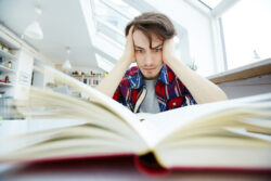Adolescente en habitación con mirada perdida, rodeado de libros y apuntes, reflejando presión interna