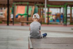Niño sentado en el borde de un patio escolar mirando una celebración desde lejos