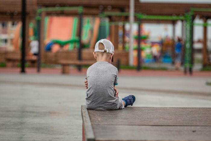 Niño sentado en el borde de un patio escolar mirando una celebración desde lejos
