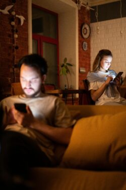 Pareja en el sofá con distancia física mirando cada uno su móvil