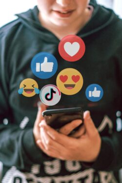 Adolescente mirando el móvil con expresión seria rodeado de iconos de redes sociales