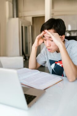 Adolescente con la cabeza entre las manos frente a un escritorio lleno de libros