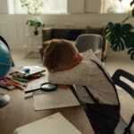 Niño pequeño sentado con aspecto cansado rodeado de material escolar