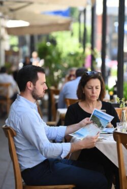 Pareja en terraza mirando cada uno hacia un lado diferente, mapa de vacaciones entre ellos, expresiones serias.