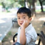 Niño con mochila escolar en suelo, sentado en banco, expresión que mezcla sonrisa y preocupación.
